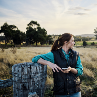 Women standing by a fence on a farm with a mobile phone in her hand