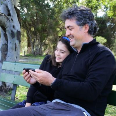 Father and daughter sitting on park bench looking at mobile phone