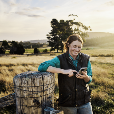 Women standing near a fence in the country, smiling whilst texting on her mobile phone 